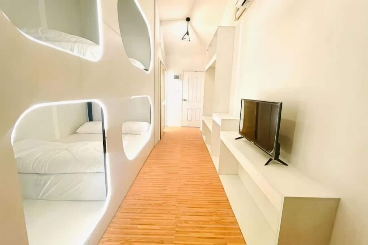 A modern hotel corridor with a wooden floor, white walls, and a flat-screen TV mounted on the wall.