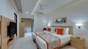 A hotel room with two beds, a TV, a desk, a nightstand, and a ceiling fan. - Ahuja Residency GCR (Gurugram)
