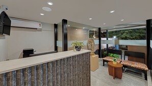 A reception area with a marble counter, a small table with a plant, and a bench with patterned cushions. - Ahuja Residency GCR (Gurugram)
