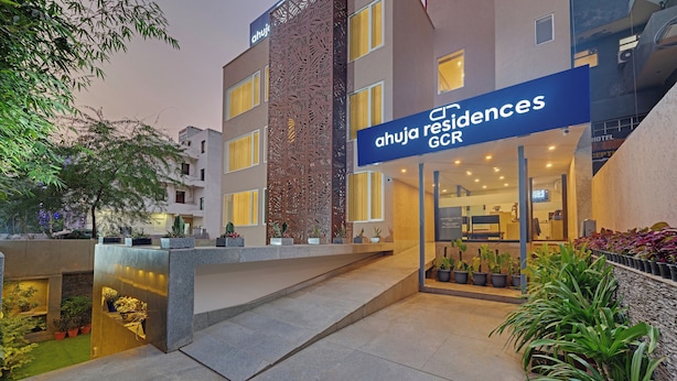 A modern hotel entrance with a sign reading "ahuja residences GCC". - Ahuja Residency GCR (Gurugram)