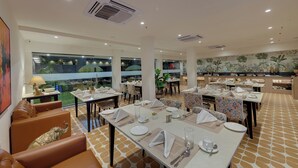 A restaurant with multiple dining tables set for guests, large windows offering views, and a modern interior design. - Ahuja Residency GCR (Gurugram)