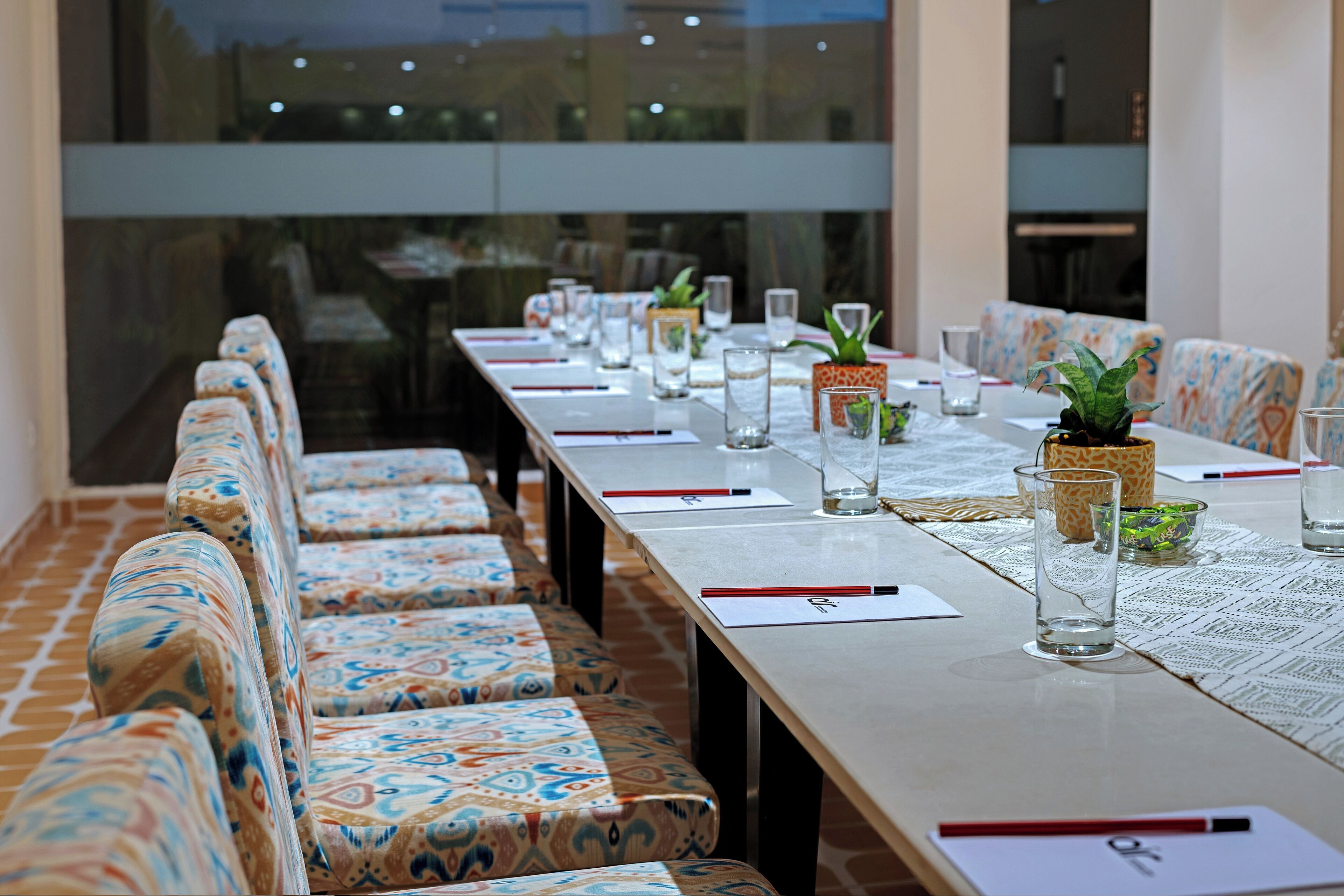 A conference room with patterned seating, a long table with name cards, glasses, and small potted plants.