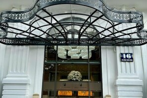 Une entrée d’immeuble dotée d’un auvent métallique décoratif et d’une enseigne indiquant le numéro 16.
