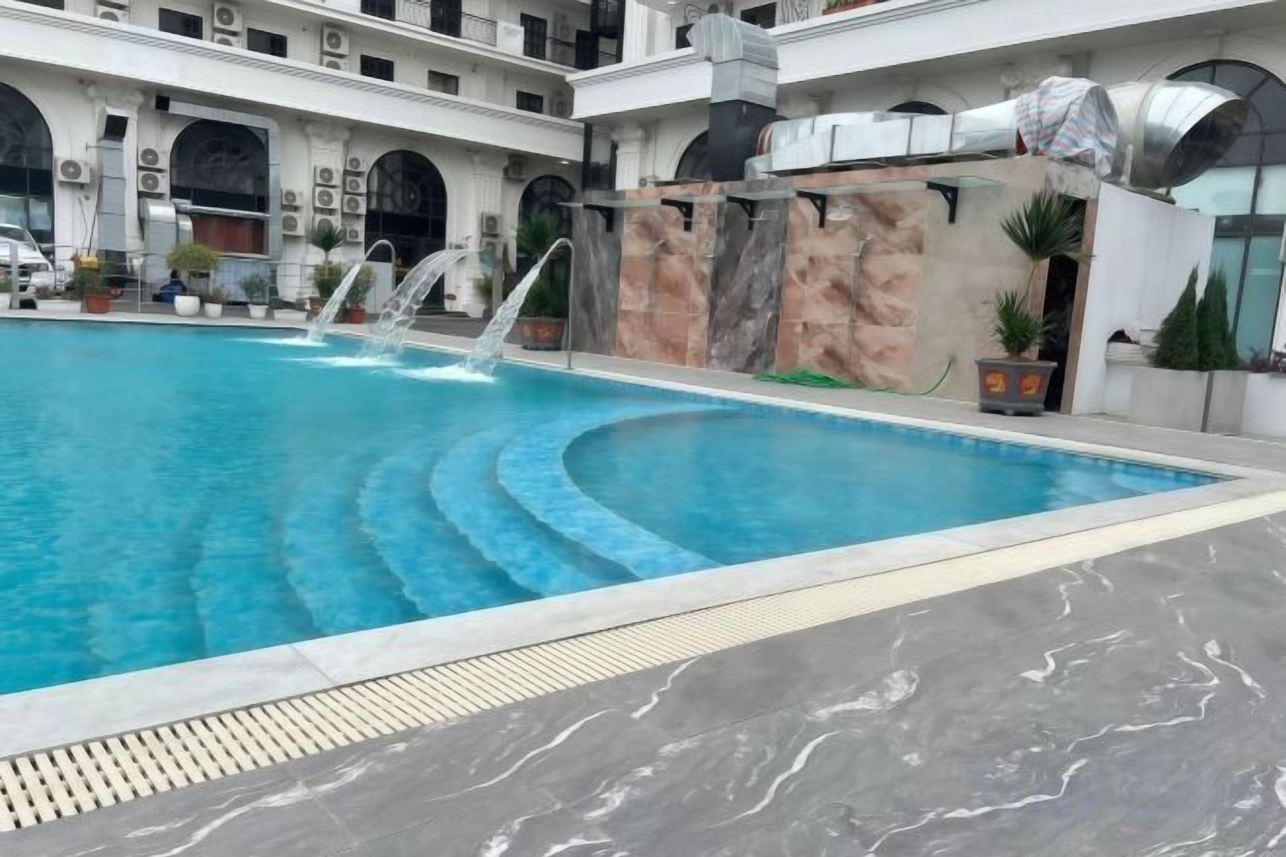 A swimming pool with a water feature, surrounded by a building with arches and a tiled floor.