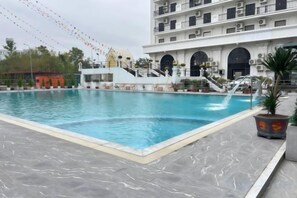 A swimming pool with a marble deck, a staircase leading to a building with multiple balconies, and a potted plant. - Royal Phoenix Hotel Bac Ninh (Bac Ninh)
