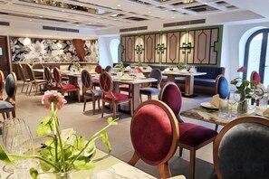 A restaurant with round tables, red and grey upholstered chairs, and a floral centerpiece. - Royal Phoenix Hotel Bac Ninh (Bac Ninh)