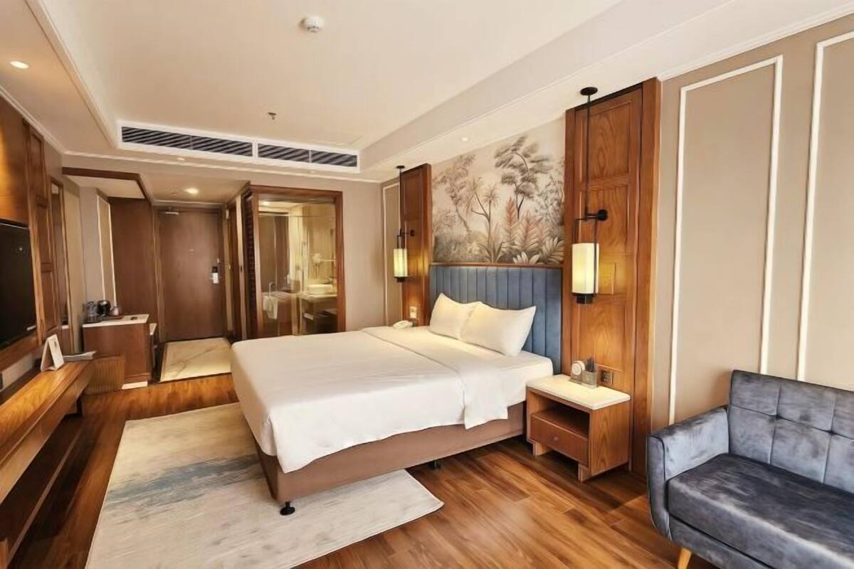 Ein Hotelzimmer mit einem großen Bett, Nachttischen, einem Fernseher, einer Sitzecke und einem Wandbild.
