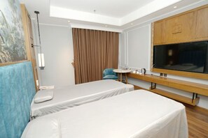 Habitación de hotel con dos camas, un escritorio, una silla, un ventanal grande y un cuadro en la pared.
