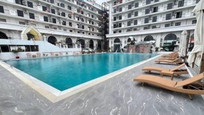 Une grande piscine intérieure avec des chaises longues, et un immeuble à plusieurs étages doté de balcons en arrière-plan.