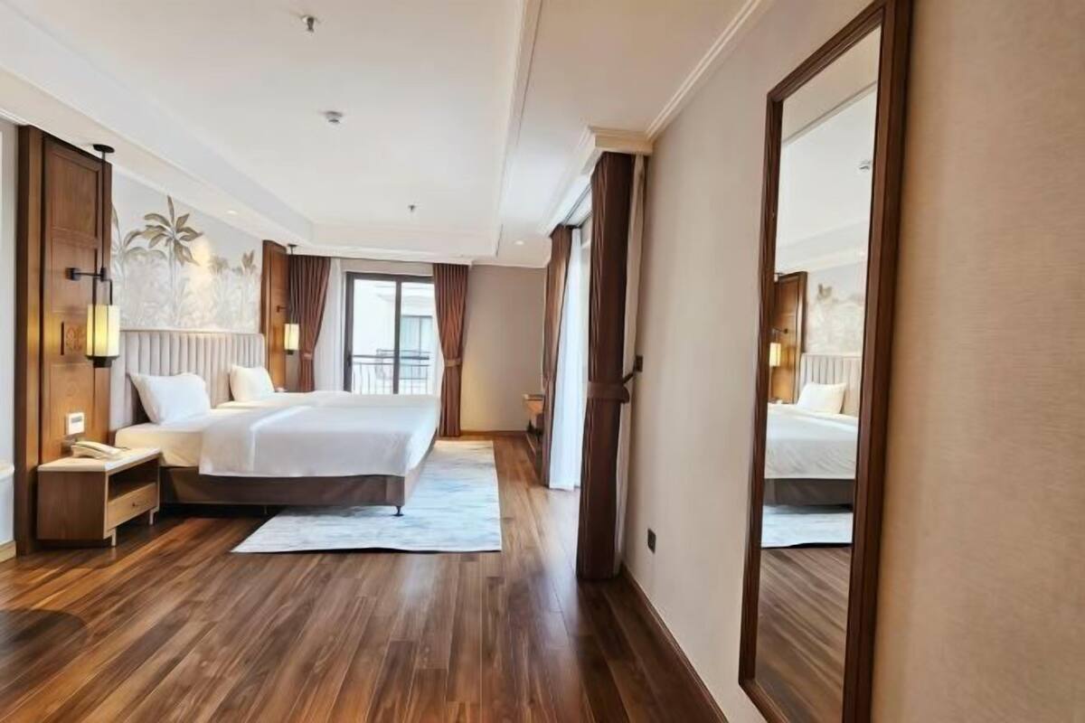 Ein Hotelzimmer mit einem großen Bett, Holzboden, einem Nachttisch, einem Spiegel und einem Fenster mit Vorhängen.