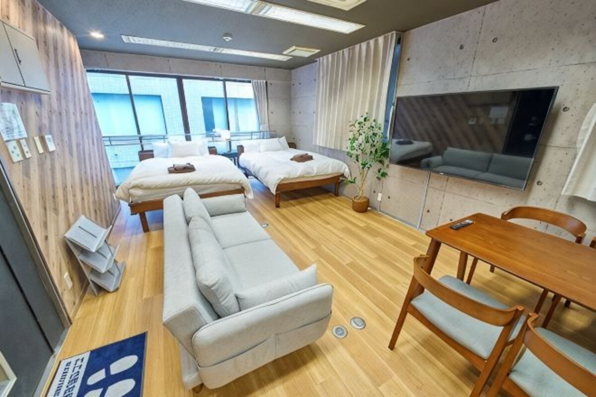 A modern hotel room with two beds, a sofa, a dining table, and a TV.