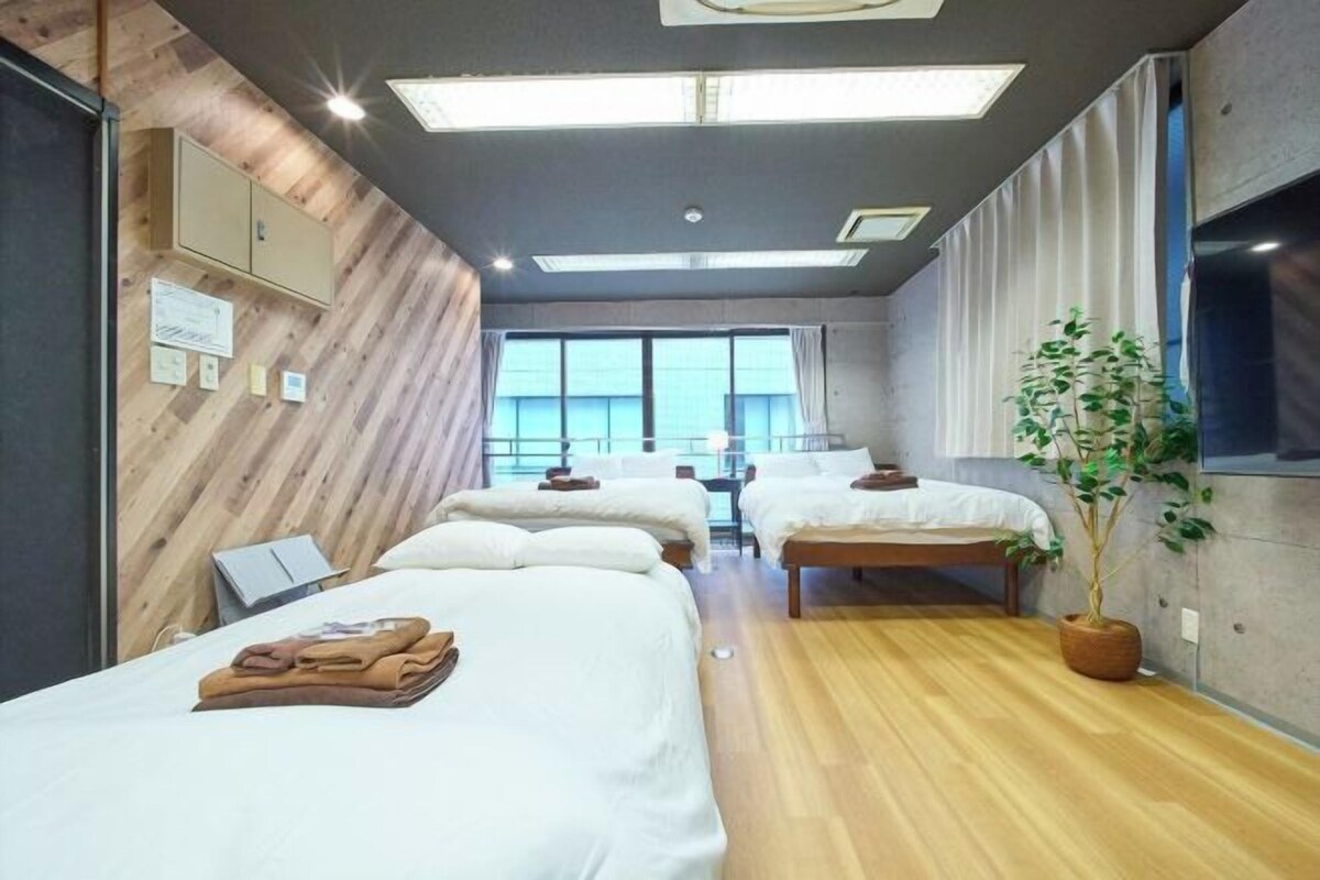 A hotel room with two beds, a wooden floor, a large window, and a plant.