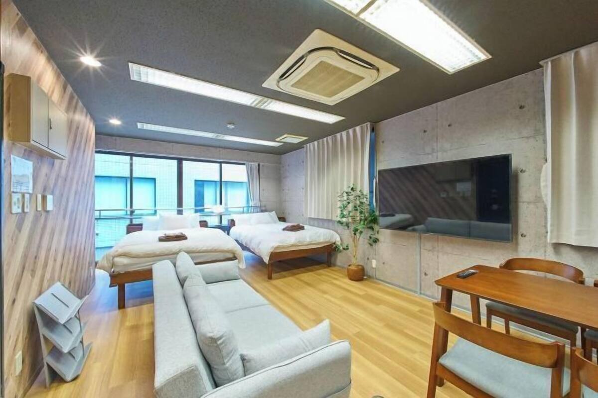 A modern hotel room with a large bed, a sofa, a dining table, and a TV.