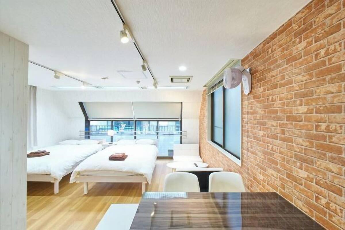 A modern hotel room with two beds, a dining table, and a large window.
