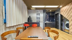 Un espace repas moderne avec une table en bois, quatre chaises, un coin bar et un lave-linge visible.