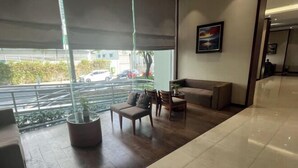 A modern hotel lobby with a large window, a seating area with a sofa and chairs, and a potted plant. - Landmark Plus Center Suite (Ho Chi Minh City)