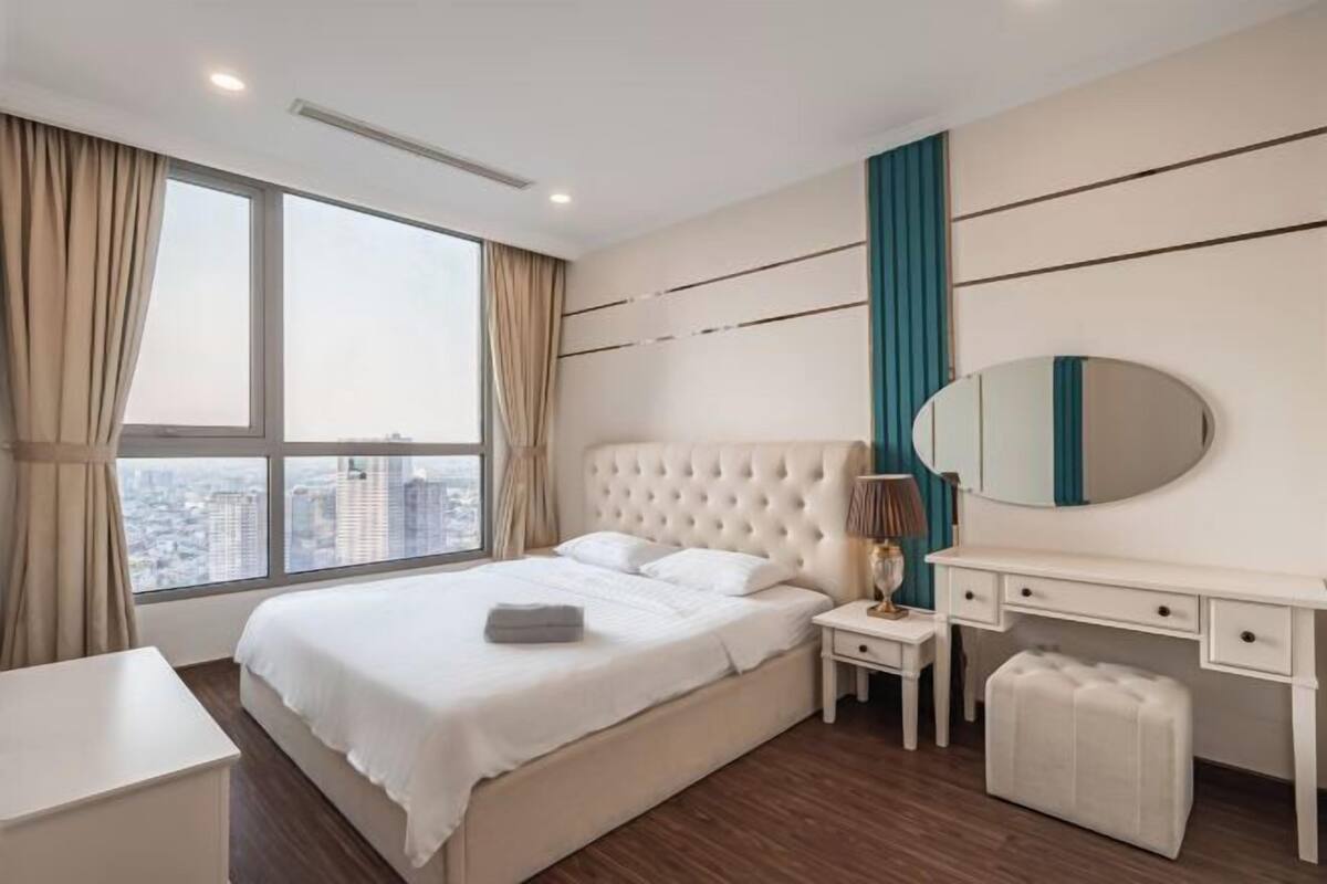 Een moderne hotelkamer met een groot bed, een nachtkastje, een spiegel en stadszicht door grote ramen.