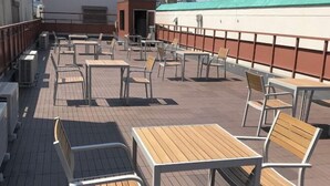 Ein Außenbereich mit Terrasse, Tischen, Stühlen, Klimaanlagen und Blick auf die Stadt.