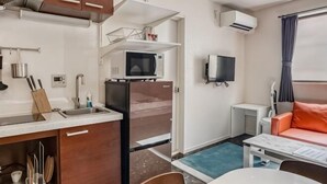 Eine kompakte Küche mit Mikrowelle, Kühlschrank und Spüle. Es gibt eine kleine Sitzecke mit Tisch und einer Couch.