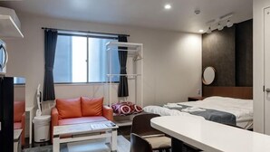 Ein Hotelzimmer mit einem Bett, einem Schreibtisch, einem Sessel, einer Couch, einem Fenster mit Vorhängen und einem Nachttisch.