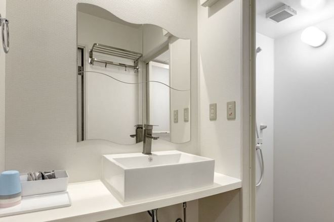 A modern bathroom with a white sink, a large mirror, and a shower area.