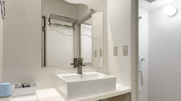 A modern bathroom with a white sink, a large mirror, and a shower area.