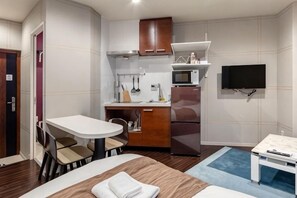 A compact hotel room with a kitchenette, a dining area, a bed, and a TV.