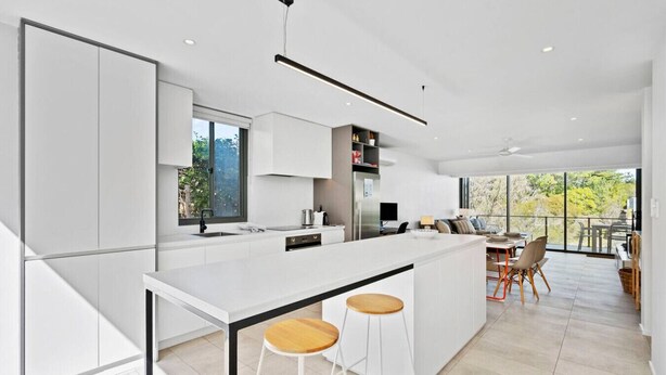 A modern kitchen with a central island, bar stools, and a dining area with a view.
