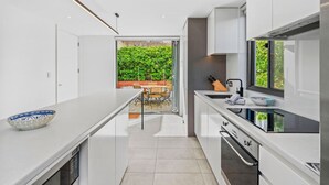 A modern kitchen with white cabinetry, a large window, and a view of a green garden.