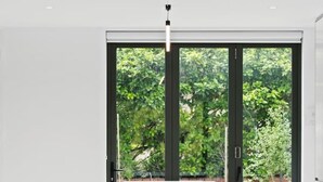 A modern dining area with a large table, multiple chairs, and a view of greenery through a glass door.
