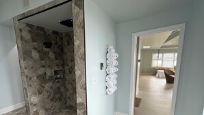 A hallway with stone flooring, a wall-mounted towel rack, and a door leading to a living area with a wicker chair and a table.