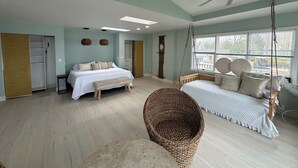 A spacious bedroom with a bed, a hanging chair, a ceiling fan, and a large window with blinds.