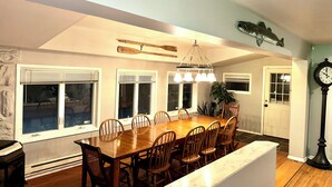 A dining area with a large wooden table, multiple chairs, a chandelier, and a clock on the wall.