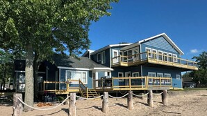A two-story beach house with a wooden deck and a balcony.