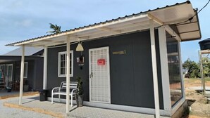 A small building with a covered porch, a door with a grid pattern, and a bench outside.