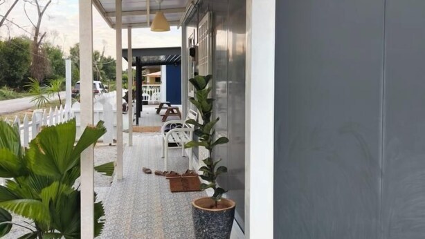 A covered outdoor area with a seating arrangement, potted plants, and a pathway leading to a building entrance.
