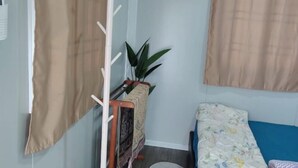 A room with a bed, a small table with a plant, a wall-mounted rack, and a curtain.