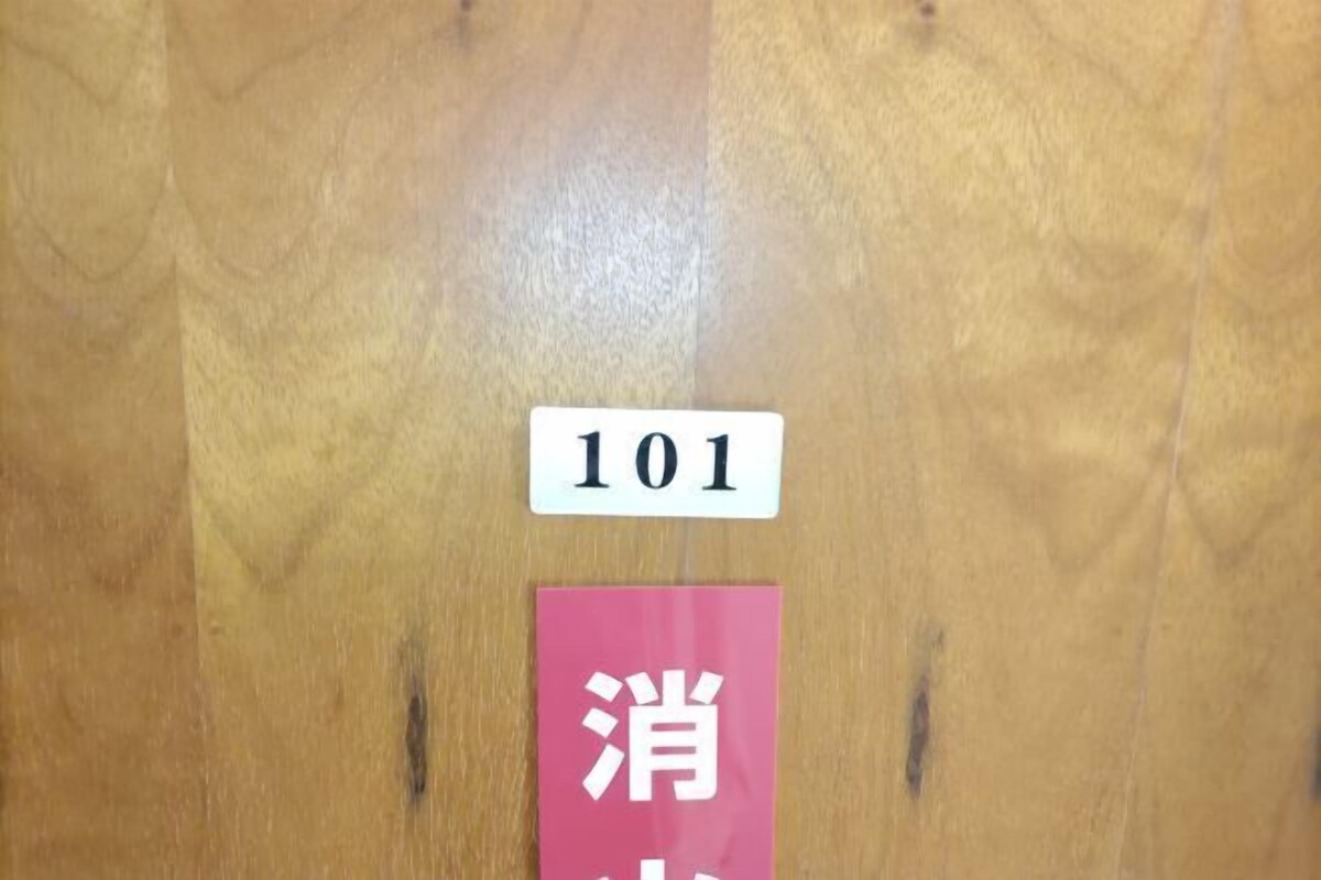 Une porte en bois avec une plaque blanche portant l’inscription « 101 » et une plaque rose avec des lettres blanches.