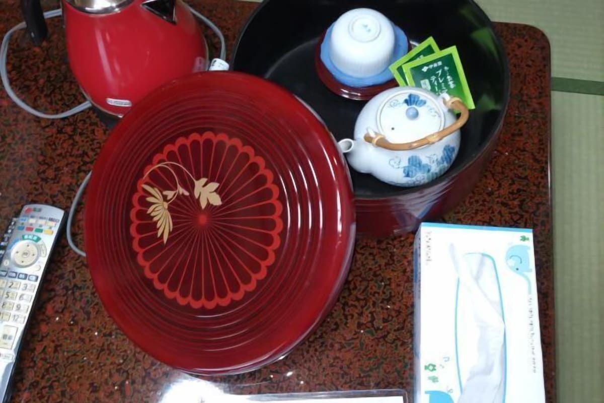 Un comptoir de cuisine avec une assiette rouge, une théière blanche, une télécommande et une boîte.