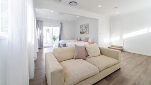 Una moderna camera d'albergo con un divano beige, un letto con due cuscini, un quadro appeso al muro e una scala che conduce a un altro livello.