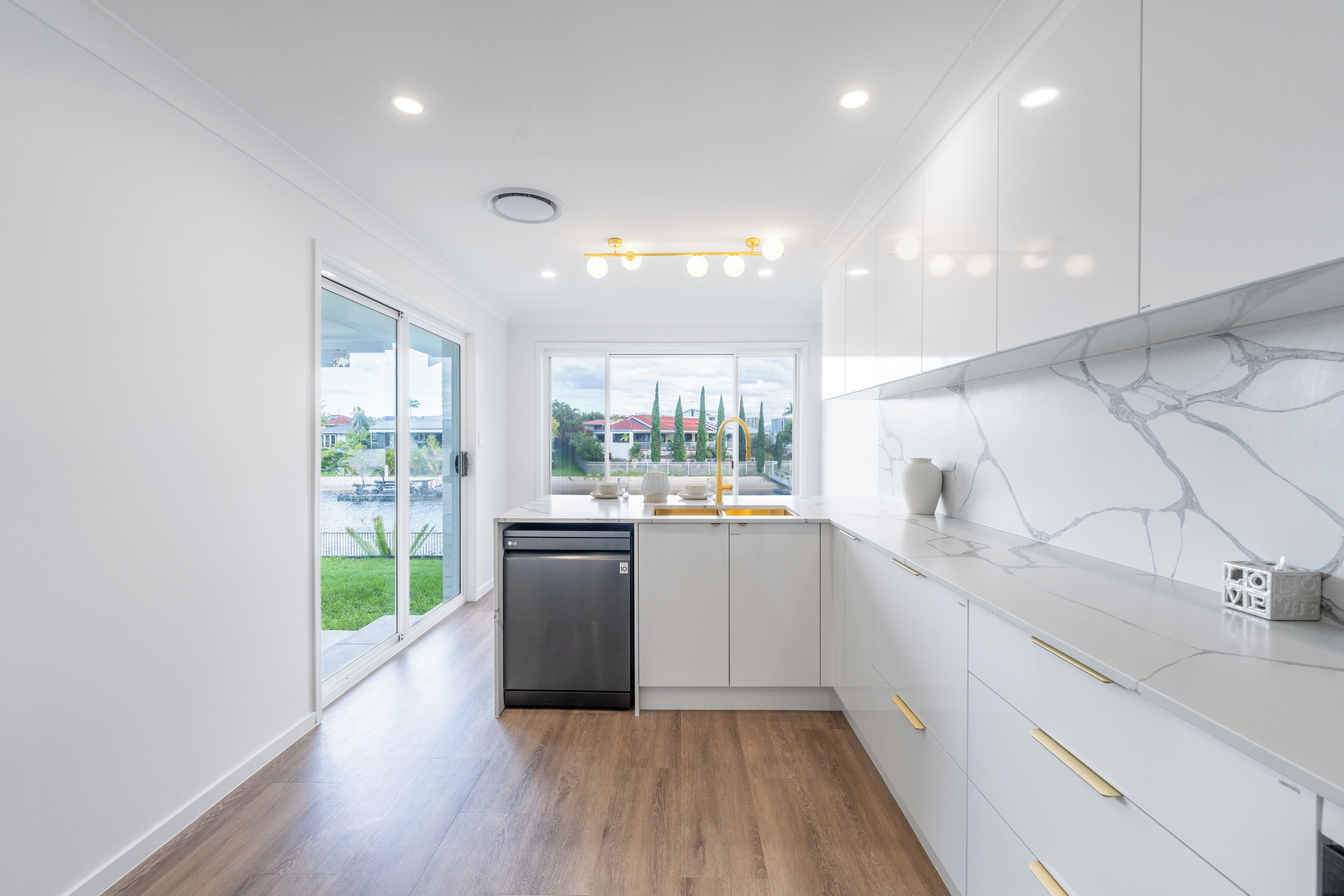 Une cuisine moderne avec des meubles blancs, un pare-feu en marbre et une vue sur l’extérieur.