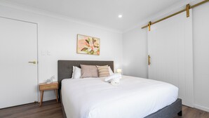 Un letto rifatto con cura, con una testiera grigia, un comodino piccolo con una lampada e un’opera d’arte appesa al muro.