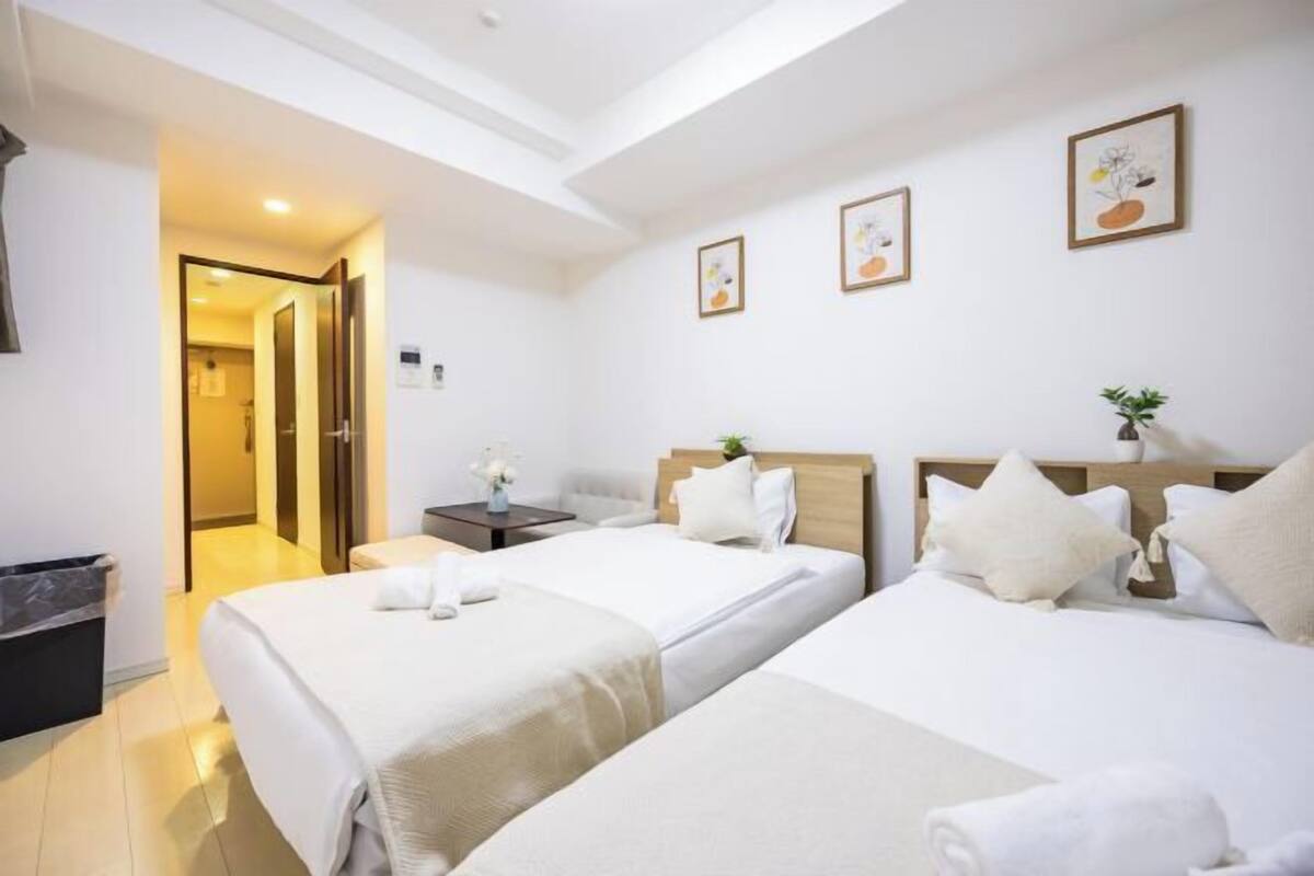 Une chambre d’hôtel avec deux lits, une table de chevet, une petite table avec un vase, et une porte donnant sur une autre pièce.