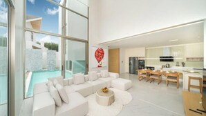 Uma sala moderna com um sofá seccional branco, uma área de jantar com móveis de madeira e uma cozinha com armários brancos.