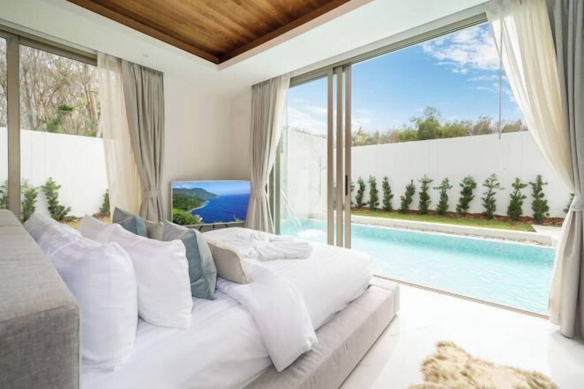 A bedroom with a large bed, a TV, and a view of a swimming pool.