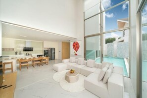 A modern interior with a living area, kitchen, and a view of a swimming pool. - 4 Bedroom Modern Pool Villa Resort near Bangtao Beach Warm Plus (Phuket)