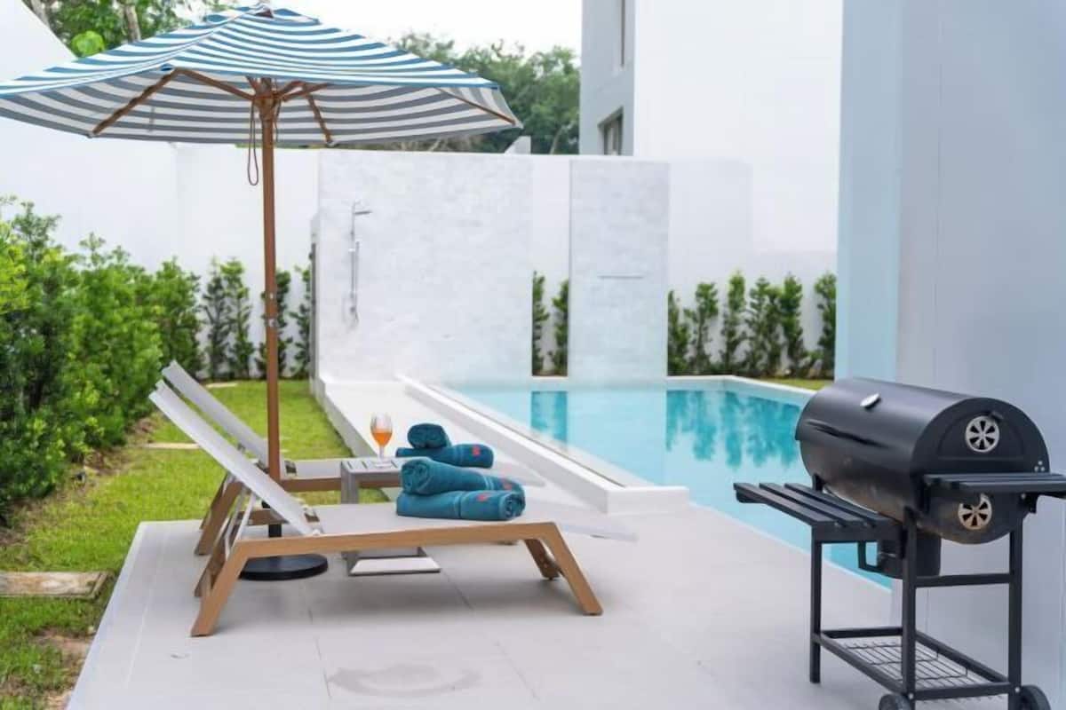 A poolside area with a lounge chair, a grill, and an umbrella.