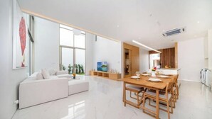 Uma sala de estar moderna com um sofá branco, uma mesa de jantar com cadeiras e uma janela grande que oferece luz natural.