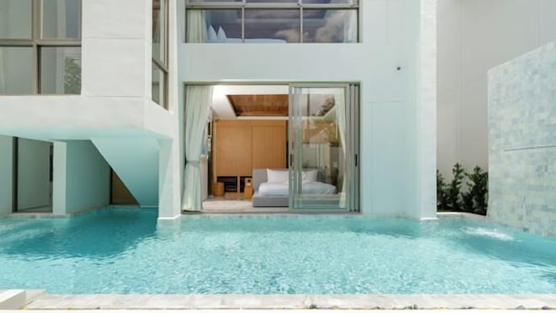 Um edifício moderno com piscina, grandes portas de vidro e interior visível com sofá e cortinas.