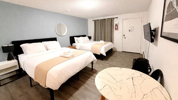 Habitación de hotel con dos camas, una mesa redonda, un escritorio, un espejo y un televisor.